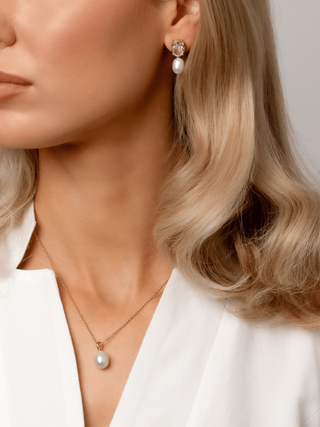 Model wearing Aurelia earrings with clear oval CZ stones and freshwater pearl drops in 14k gold plating