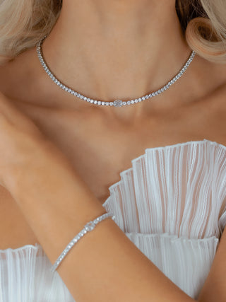 White gold tennis necklace and matching bracelet with clear CZ stones and oval centre design, worn with white pleated dress