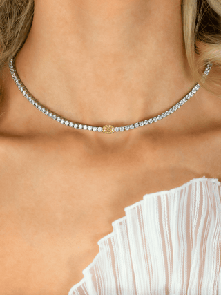 Close-up of model wearing Aurelia white gold plated tennis necklace with central lemon yellow oval CZ stone and white pleated dress