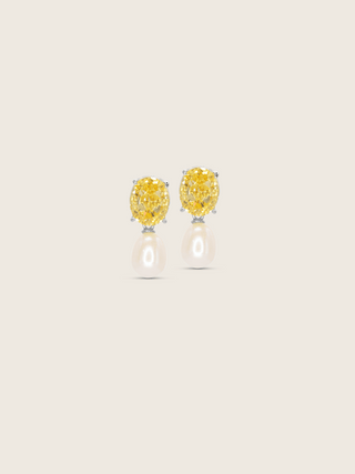 White gold plated Aurelia earrings with oval yellow CZ stones and freshwater pearl drops on neutral background