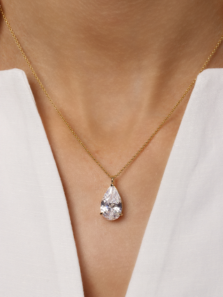 Close up of Aurora Pendant Necklace with large pear shaped cubic zirconia on a fine 14k gold plated chain, styled with white V neckline