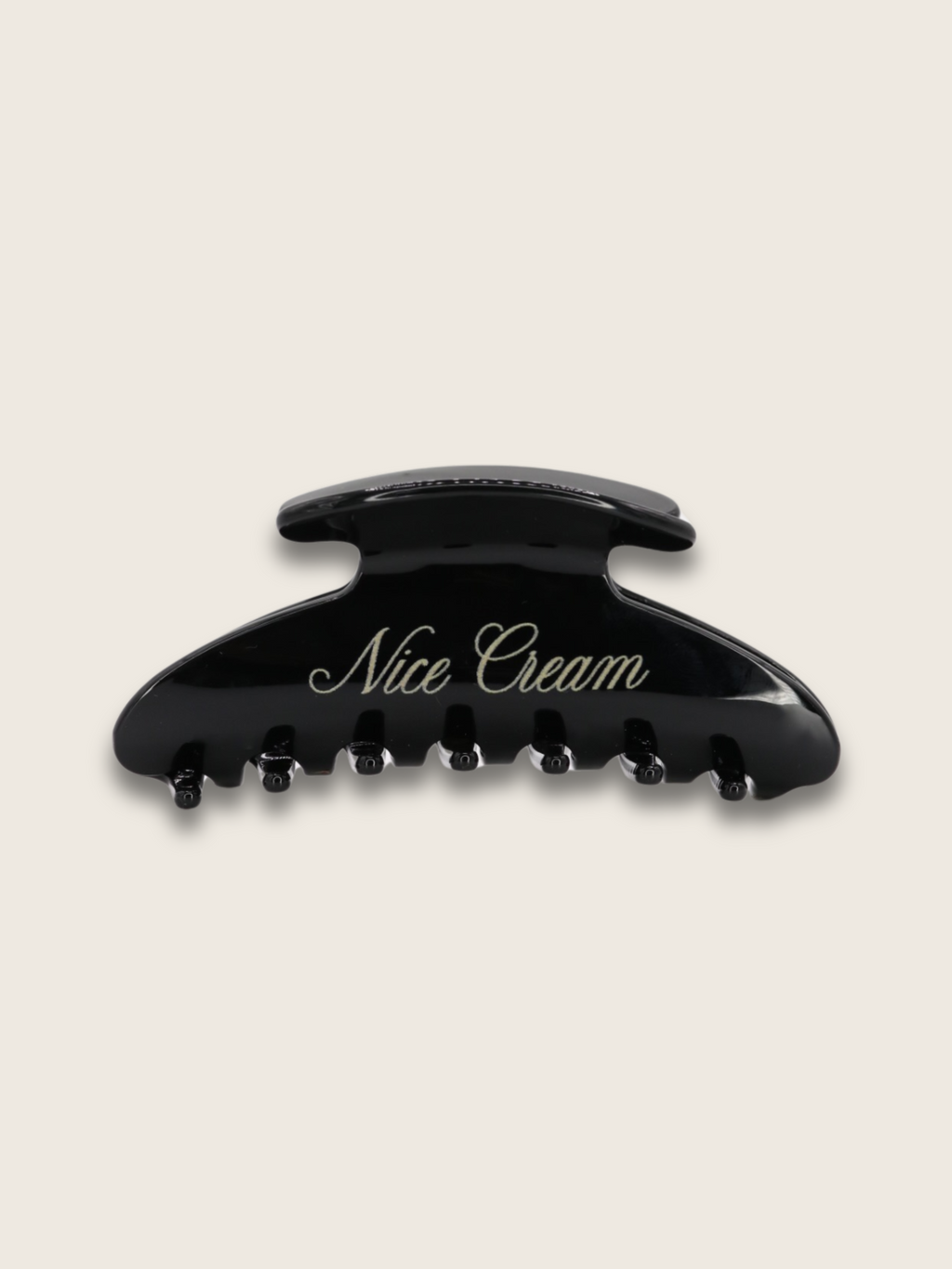 Flatlay of a shiny black claw hair clip, with the brand name written on the side, displayed on a plain white background