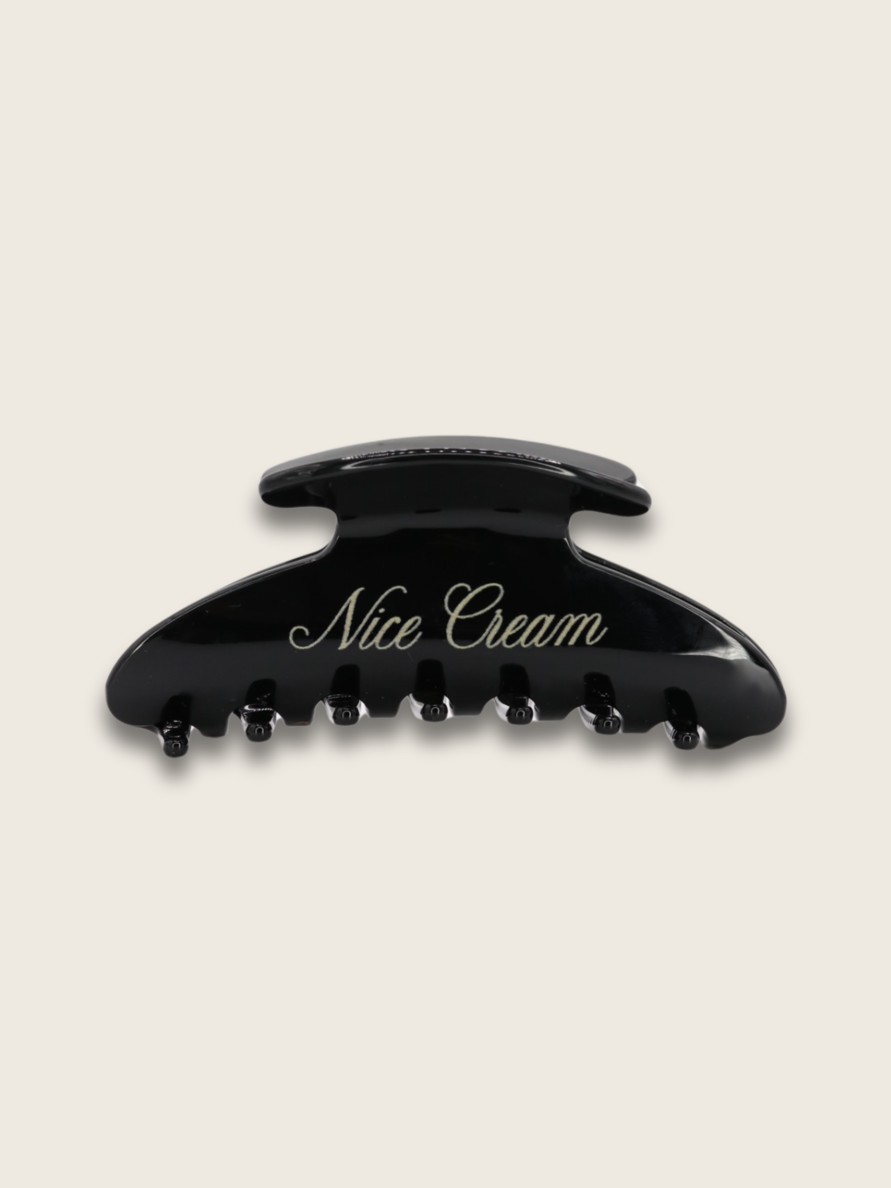Flatlay of a shiny black claw hair clip, with the brand name written on the side, displayed on a plain white background
