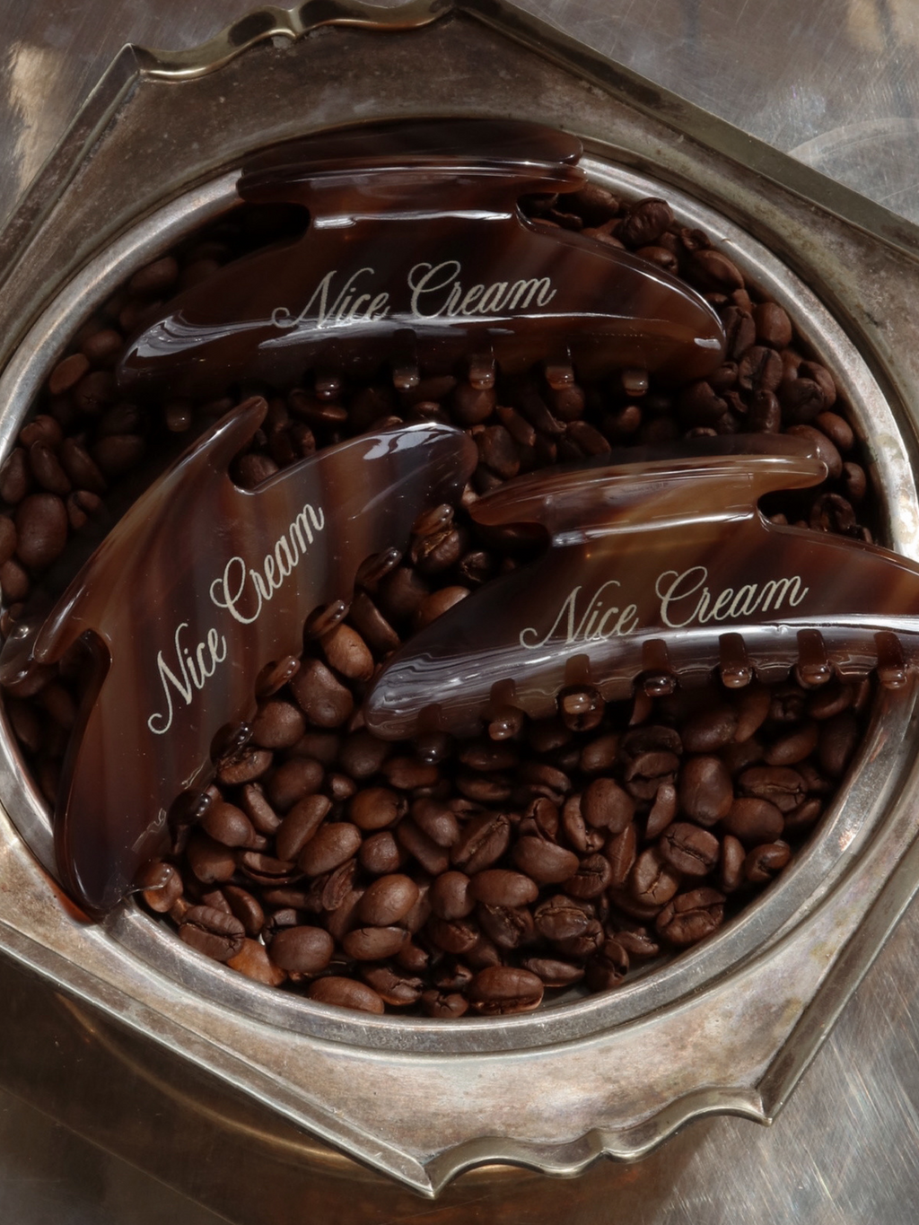 Overhead view of three cappuccino-coloured claw hair clips nestled in a silver dish filled with coffee beans