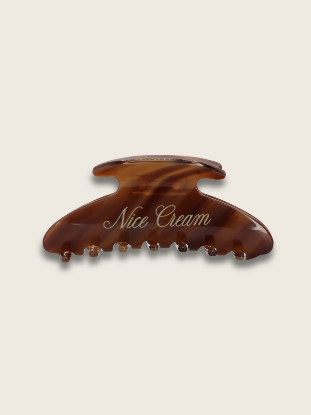 Flat-lay of a cappuccino-coloured claw hair clip with brand name in elegant font, displayed on a plain white background