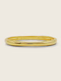 Christy bangle in 14k gold plating with smooth, polished finish on neutral background
