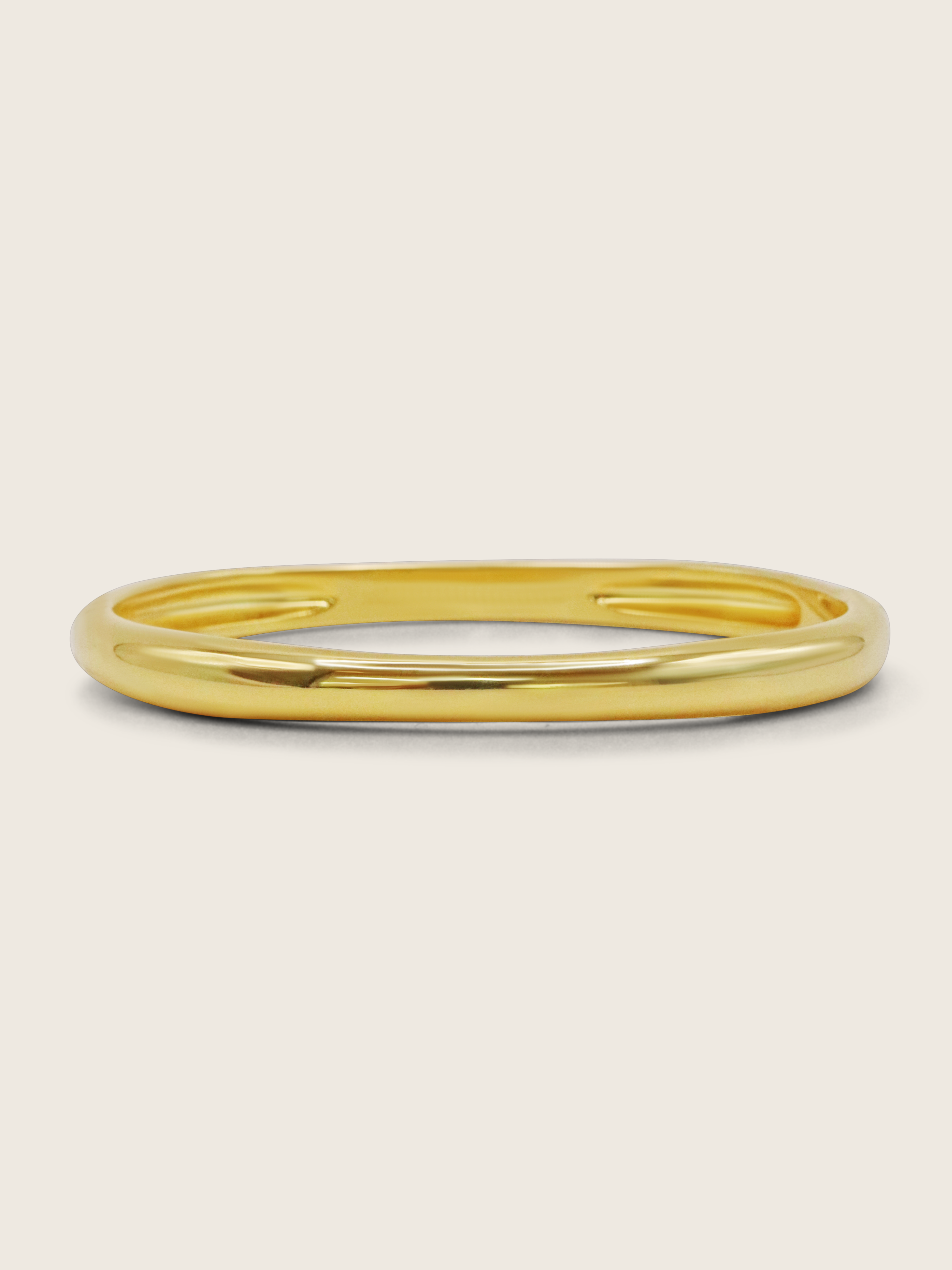 Christy bangle in 14k gold plating with smooth, polished finish on neutral background