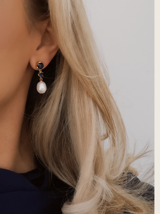Clarissa Earrings in 14k gold plating with deep blue cubic zirconia stones and pearl drop, close-up on ear side view