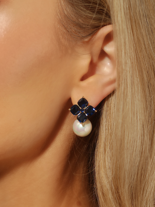 Close up of ear wearing 14k gold plated hydrangea earrings with translucent deep blue stones and shell pearl