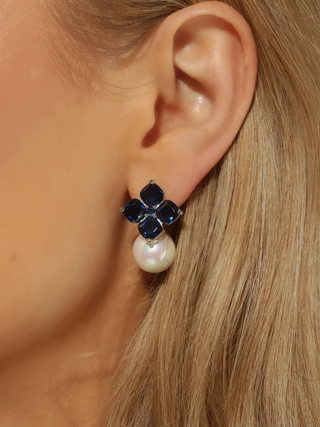 Close up of ear wearing white gold plated hydrangea earrings with translucent deep blue stones and shell pearl