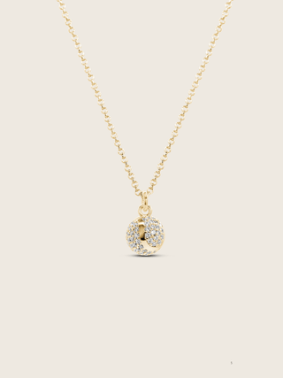 Gold plated tennis ball pendant necklace with pavé CZ stones on neutral background