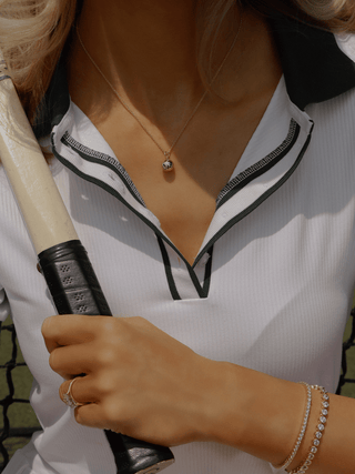 Model wearing gold plated semi pavé tennis ball necklace with sportswear on tennis court