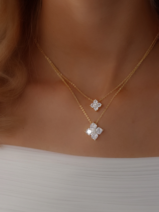 Close-up, diagonal view of a model’s neckline wearing both the Crystal Hydrangea Necklace and the Mini Crystal Hydrangea Necklace in gold plating, styled with a white dress to highlight the size and design contrast between the two pendants.