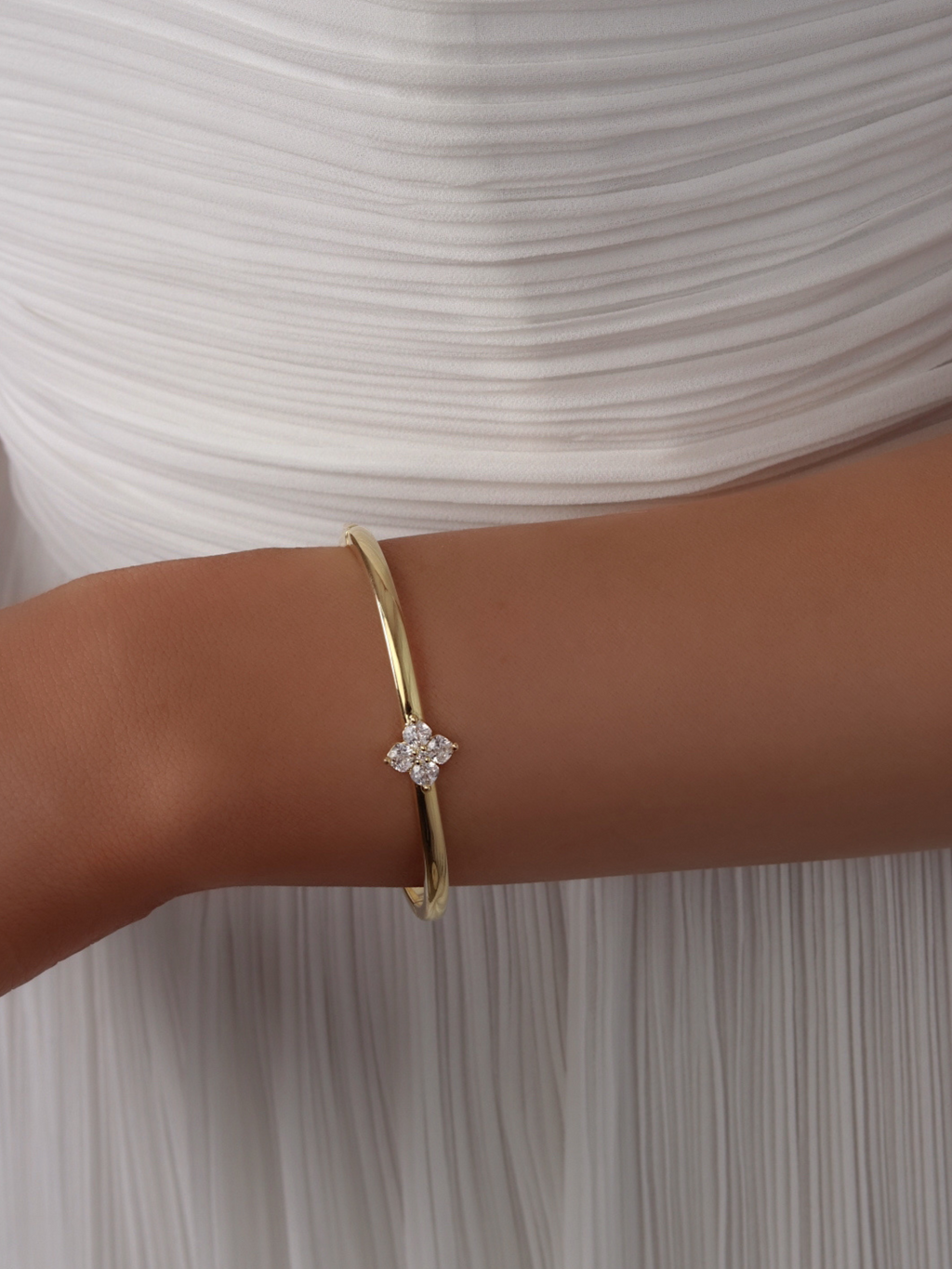 Close-up of the Crystal Hydrangea Bangle on a model’s wrist, paired with a white dress, showcasing the sparkling hydrangea stone set on a gold-plated bangle.