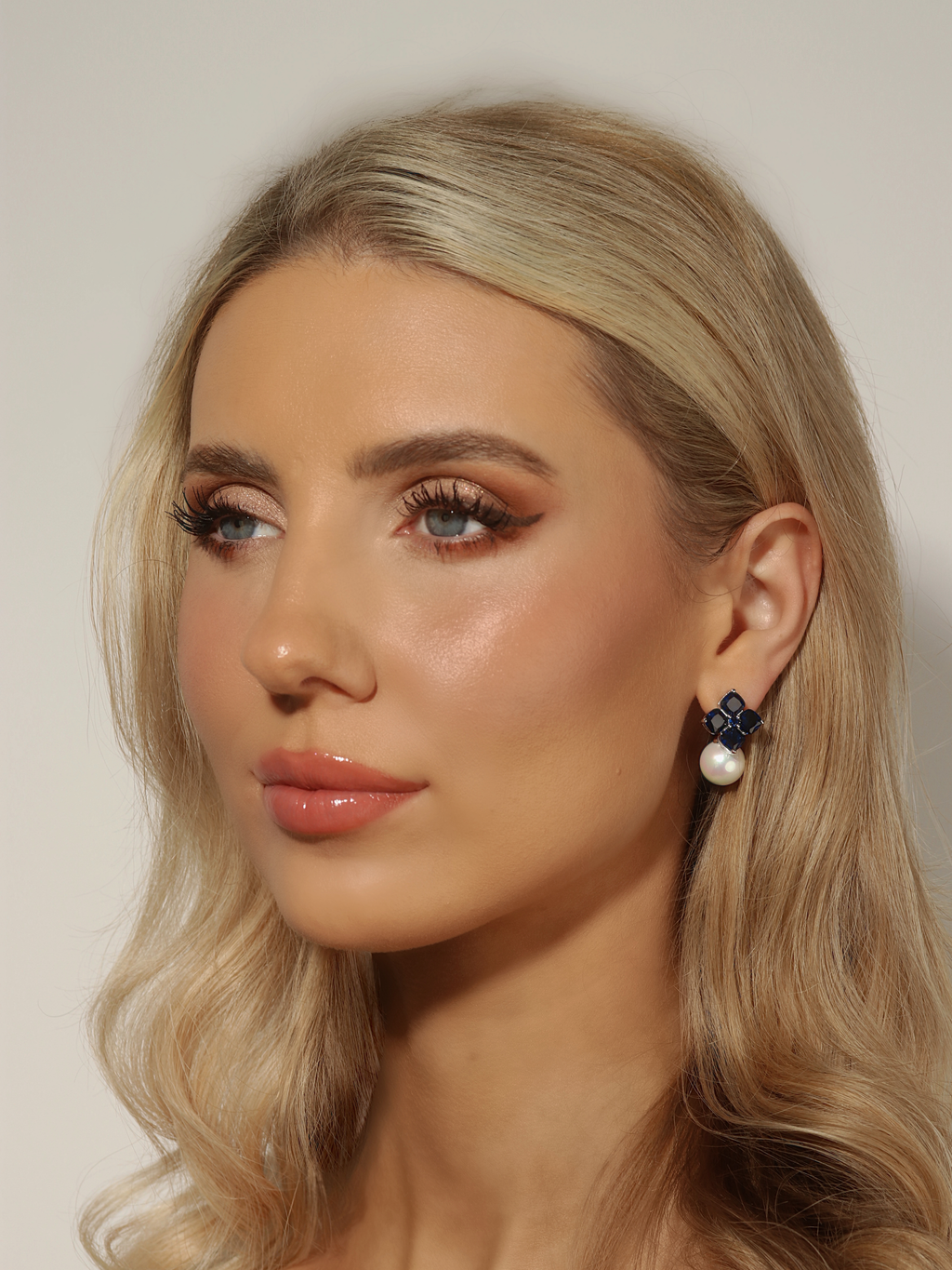 Woman wearing white gold plated hydrangea earrings with translucent deep blue stones and a shell pearl drop