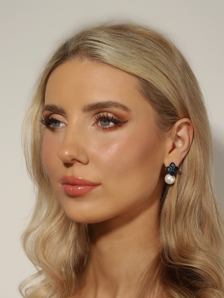 Woman wearing white gold plated hydrangea earrings with translucent deep blue stones and a shell pearl drop