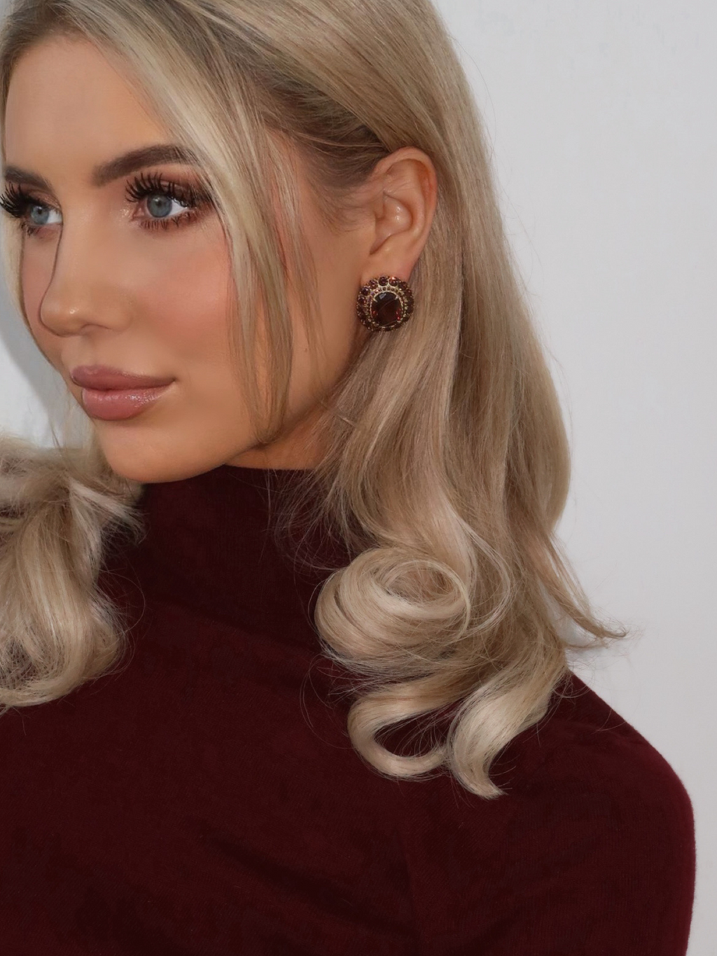  Model wearing Diana earrings with wine CZ stones, styled with soft curls and a deep burgundy top