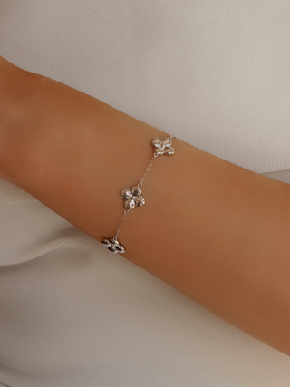Florence bracelet featuring multiple polished hydrangea-inspired flowers on a delicate white gold plated sterling silver chain, worn on the model’s wrist against a white dress background for a refined, floral-inspired look.