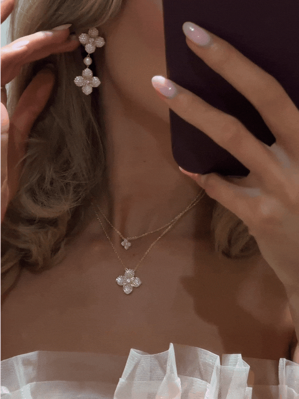 Stacked hydrangea necklaces in gold with light pink CZ, worn together to showcase mini and full pendant layering, paired with matching earrings in a mirror selfie GIF