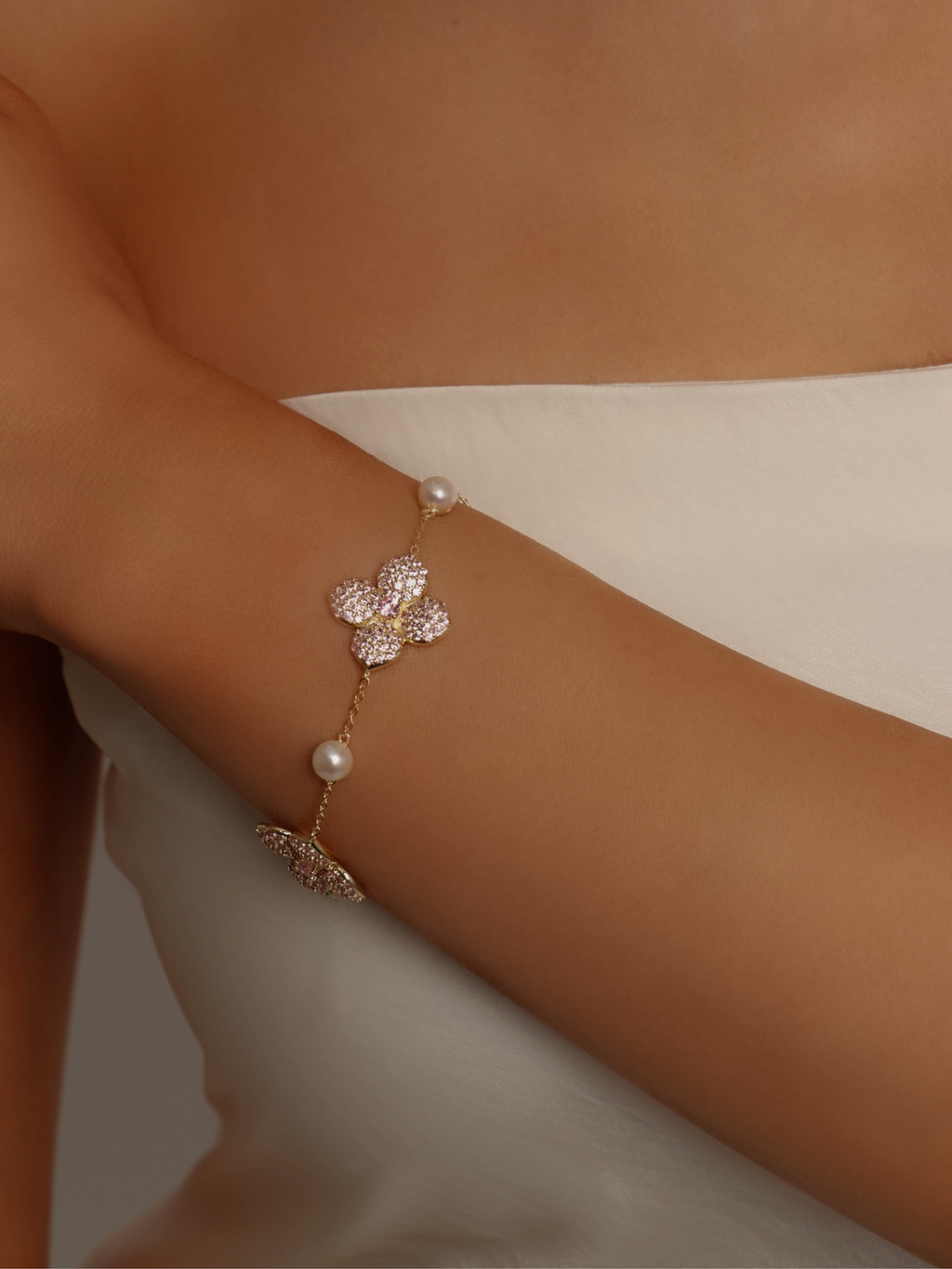 Gold hydrangea bracelet with light pink CZ stones and pearls, worn on wrist with white dress