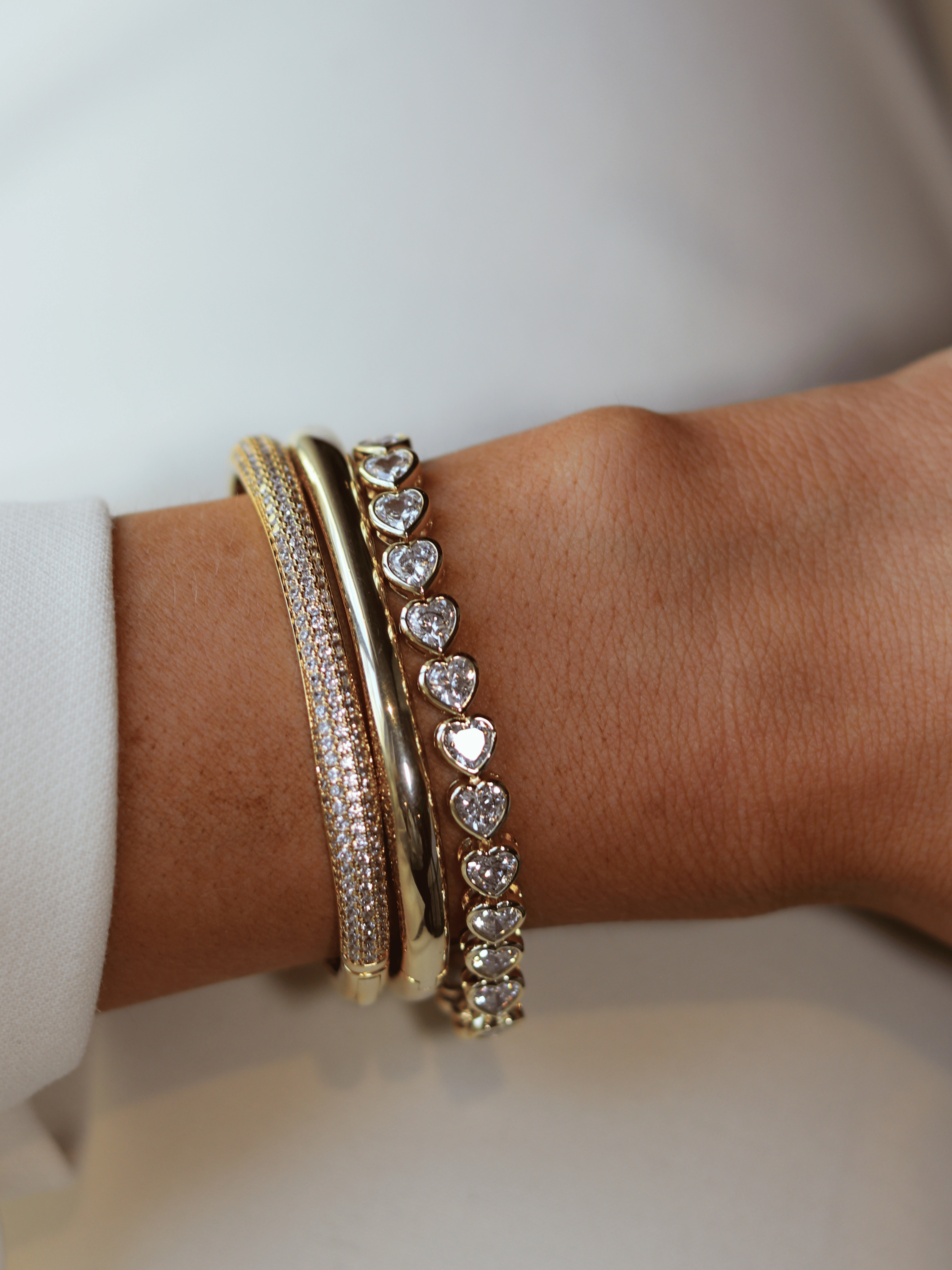 Juliette bracelet in gold with heart-shaped CZ stones, worn stacked with bangles on wrist for a radiant, layered look with refined sparkle