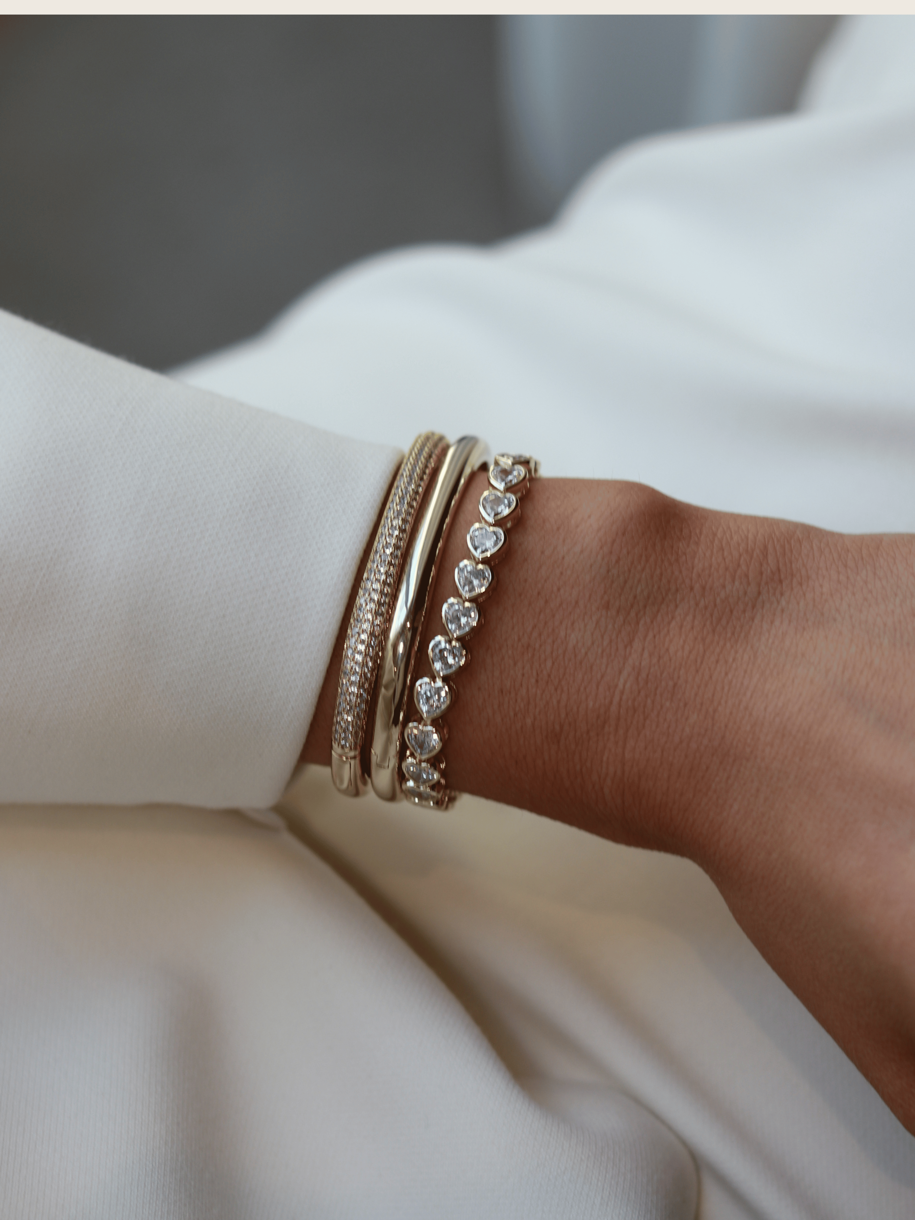  Gold heart tennis bracelet worn with polished and pavé bangles, styled on wrist in natural light for an elegant, high-impact stack