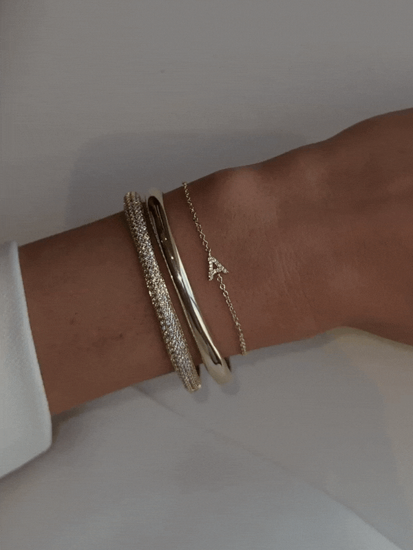 Shimmering GIF of stacked wrist featuring gold Love Letter bracelet with ‘A’ CZ initial charm, styled with contrasting bangles for an elegant mixed-texture finish
