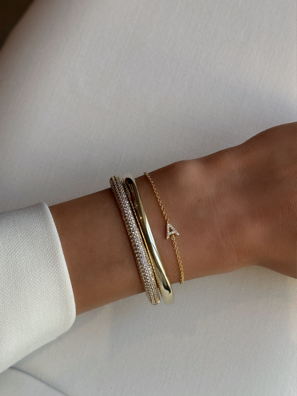 Love Letter bracelet in gold with ‘A’ initial in CZ, styled with polished and pavé Christy bangles for a chic layered wrist look