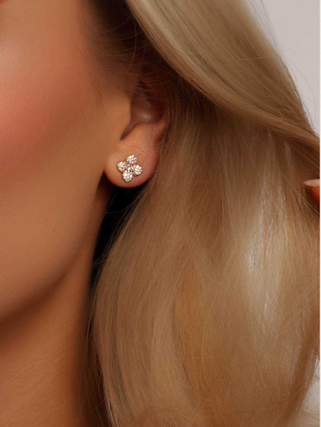 Close-up of mini hydrangea stud earring in gold with light pink CZ stones, worn on ear with soft blonde hair, ideal for refined everyday or occasion wear