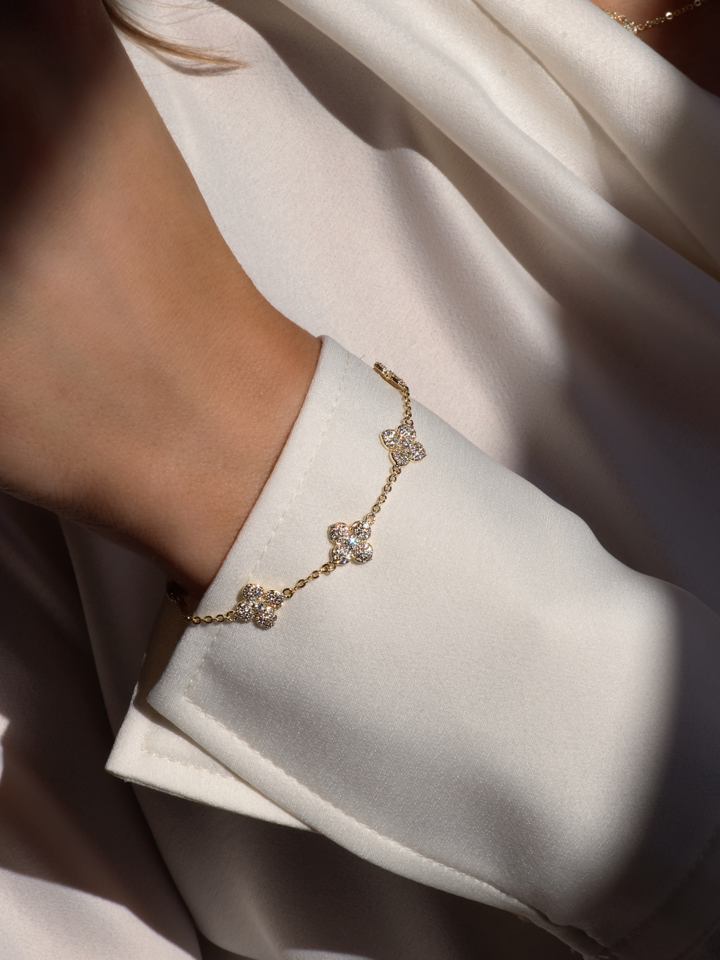 Close up of gold Multi Mini Hydrangea bracelet worn over satin cuff, sparkling in natural light
