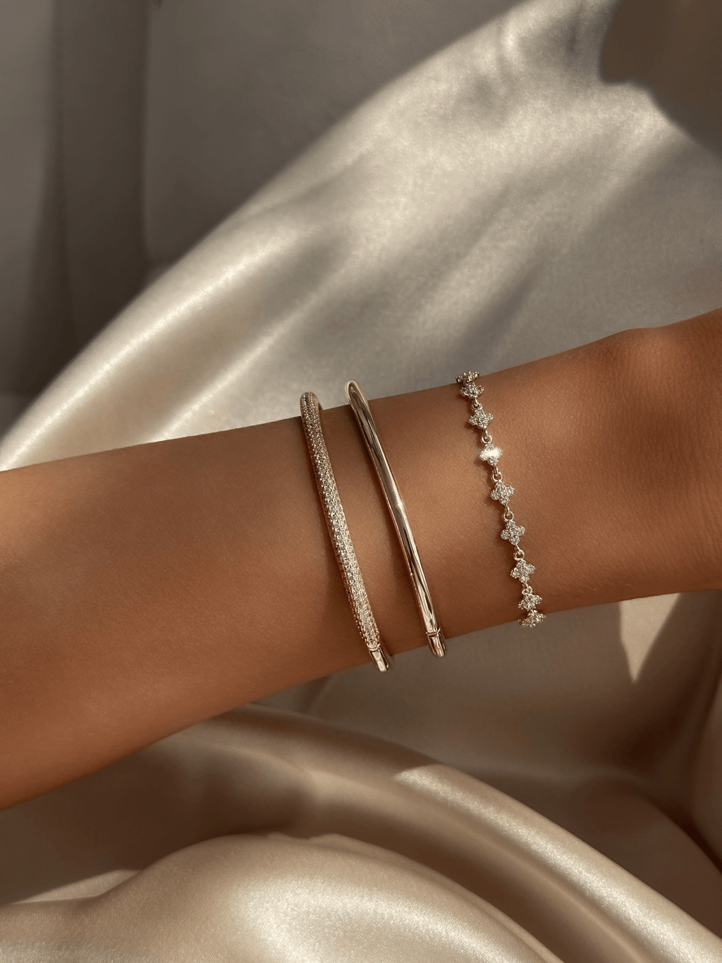 Plain gold plated slim Christy bangle stacked with pavé Christy bangle and Micro Hydrangea Bracelet on satin background. Minimalist gold bracelet layering for refined everyday styling.