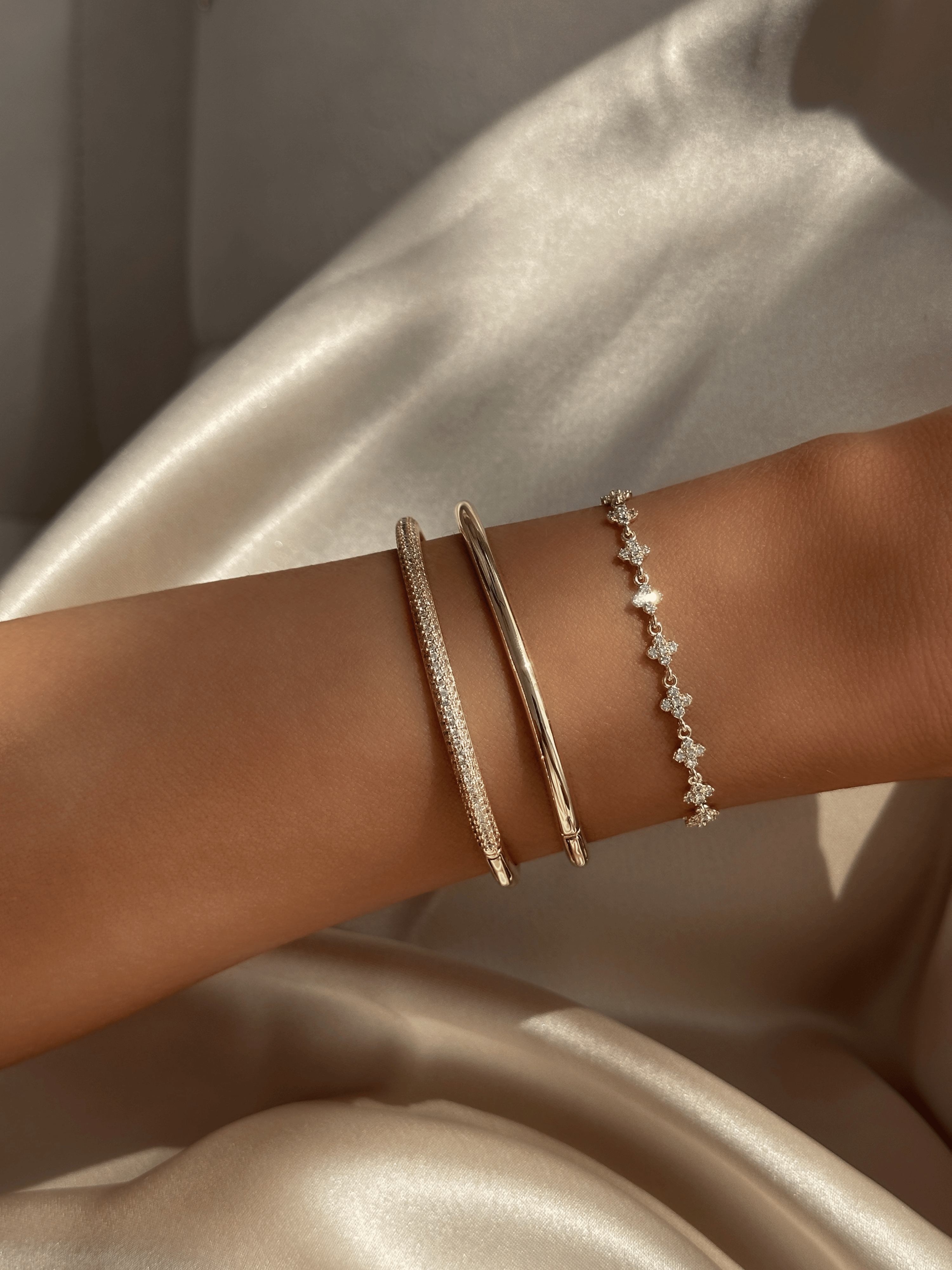 Plain gold plated slim Christy bangle stacked with pavé Christy bangle and Micro Hydrangea Bracelet on satin background. Minimalist gold bracelet layering for refined everyday styling.