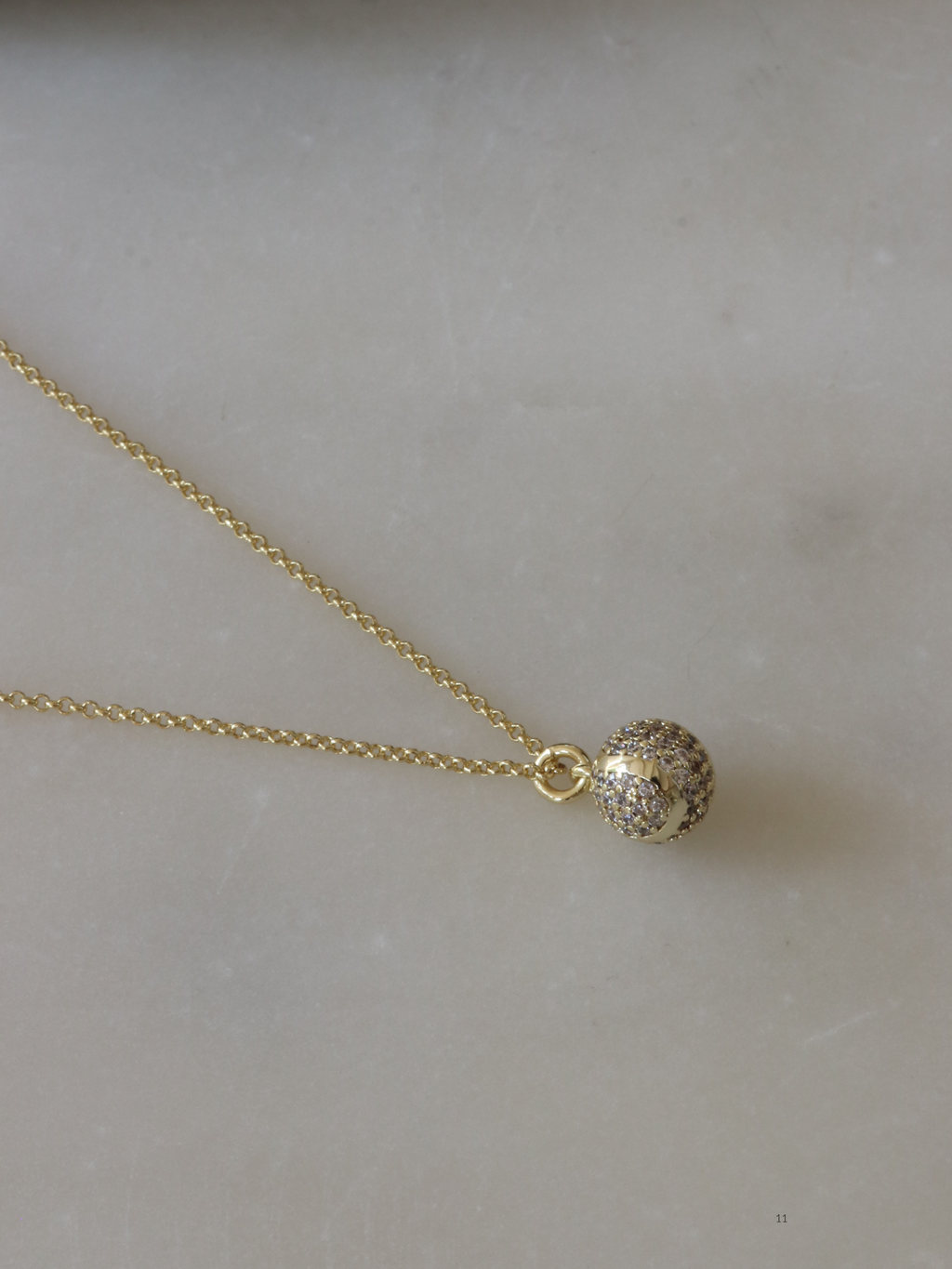 Gold plated tennis ball pendant necklace fully pavé set with CZ stones, displayed on marble background