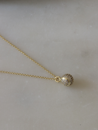 Gold plated tennis ball pendant necklace fully pavé set with CZ stones, displayed on marble background