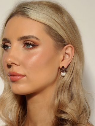 Woman wearing 14k gold plated hydrangea earrings with translucent cinnamon cubic zirconia stones and shell pearl drop