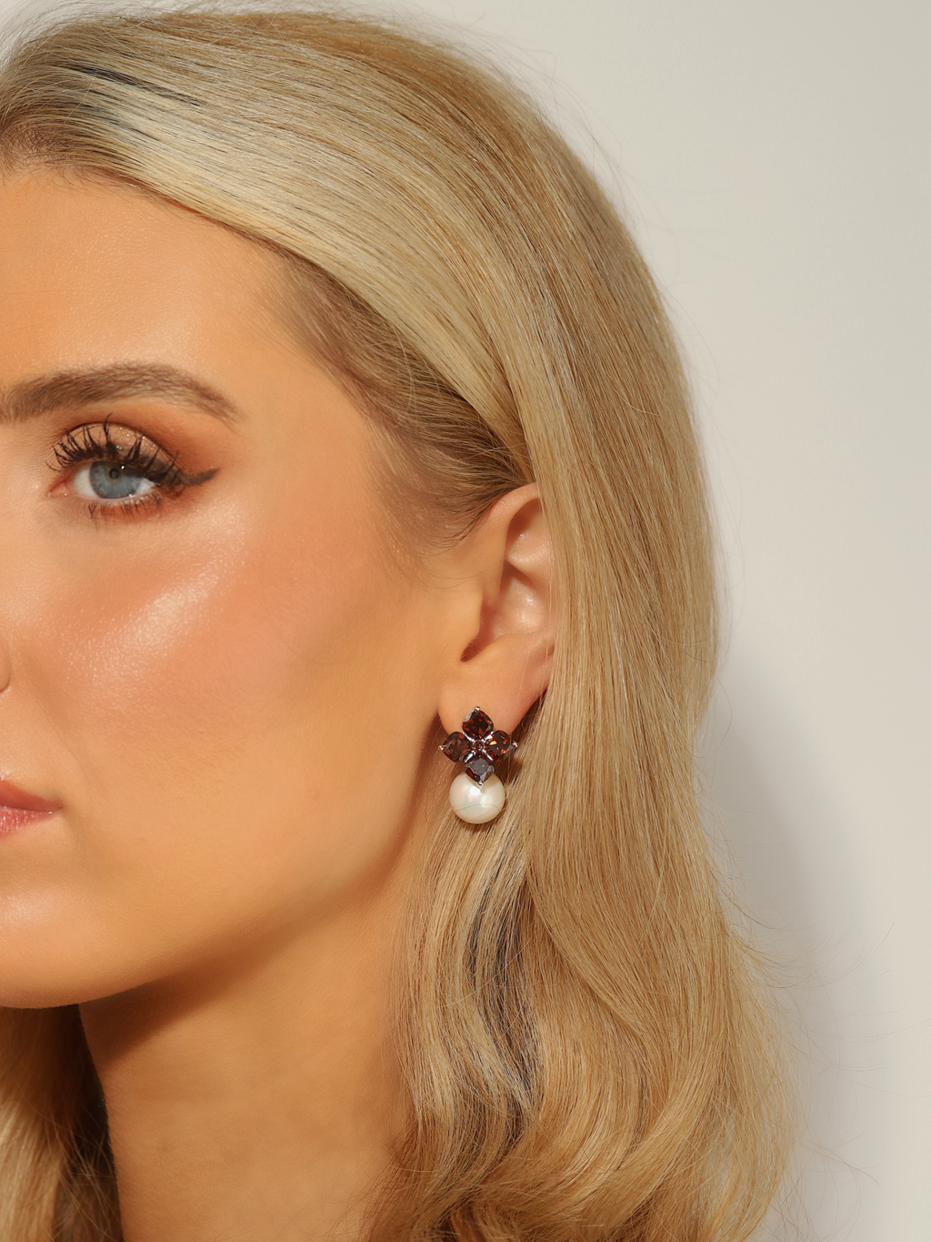 Woman wearing white gold plated hydrangea earrings with translucent cinnamon cubic zirconia stones and shell pearl drop