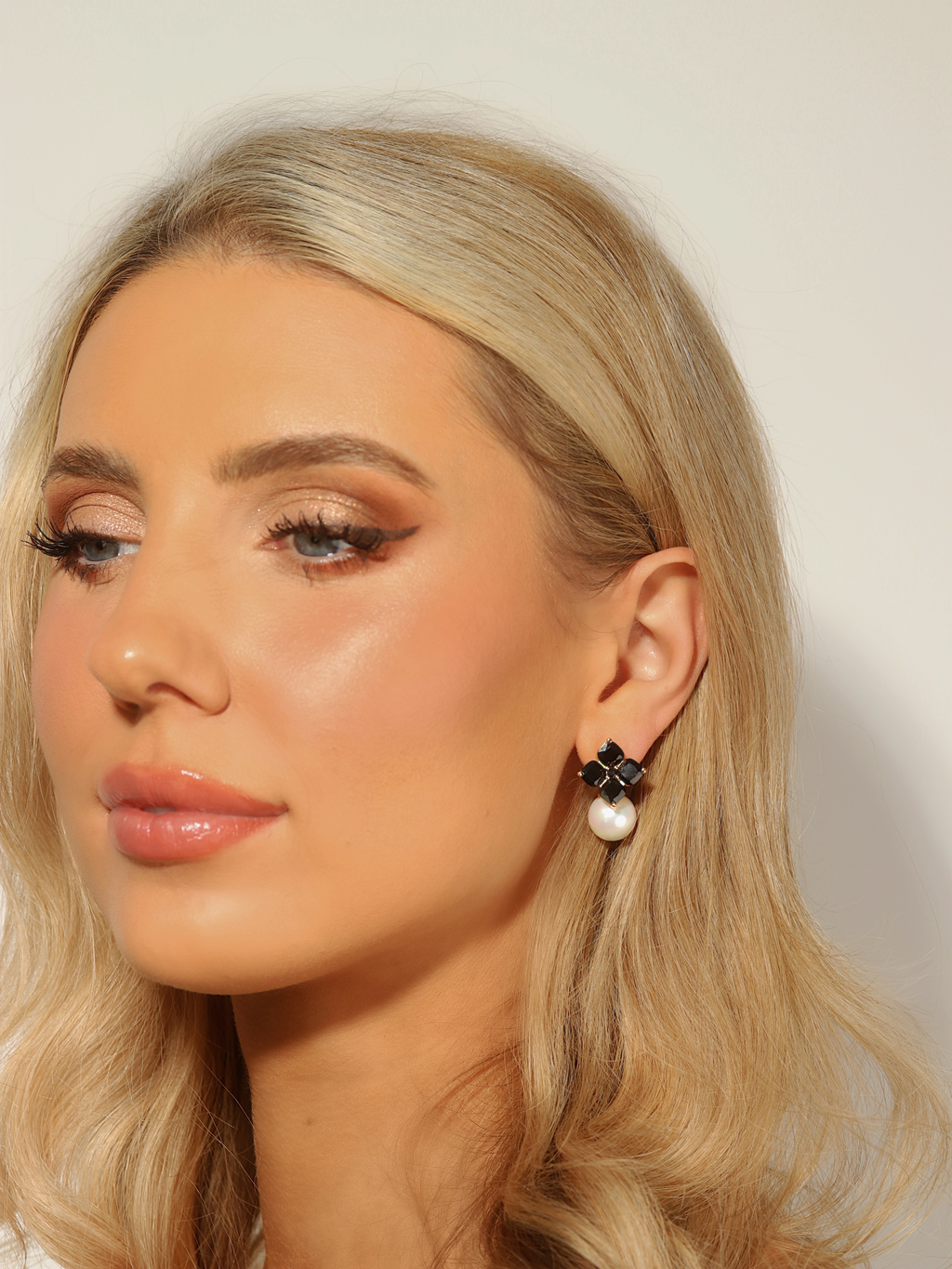 Woman wearing 14k gold plated hydrangea earrings with black cubic zirconia stones and shell pearl drop