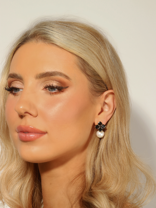 Woman wearing 14k gold plated hydrangea earrings with black cubic zirconia stones and shell pearl drop