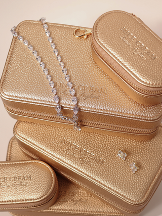 Champagne jewellery case collection with large and small cases stacked, crystal necklace draped across and stud earrings displayed.
