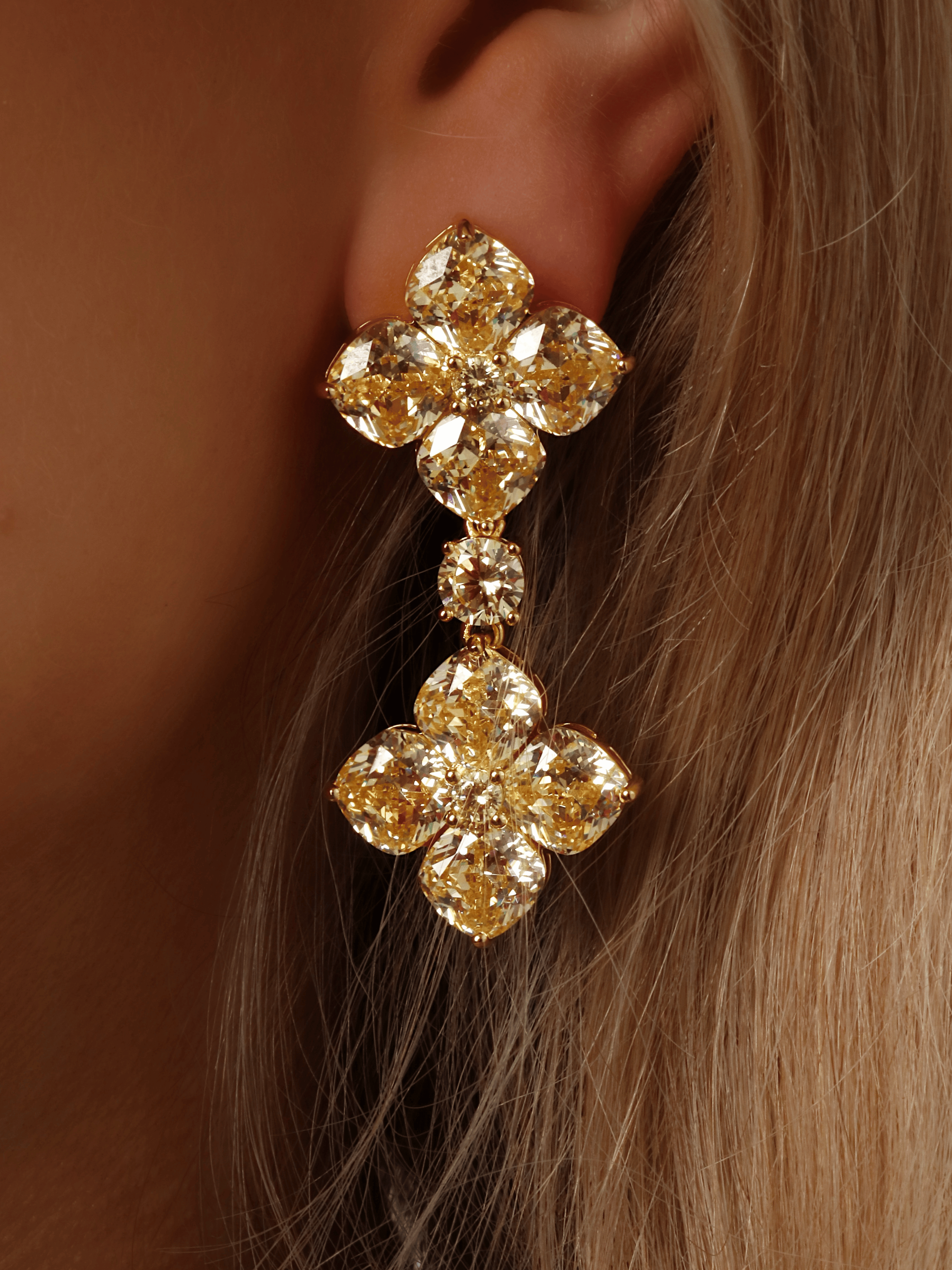 Close-up of gold-plated 5cm drop earrings with double lemon CZ hydrangea clusters and central cushion-cut connector, worn on model’s ear