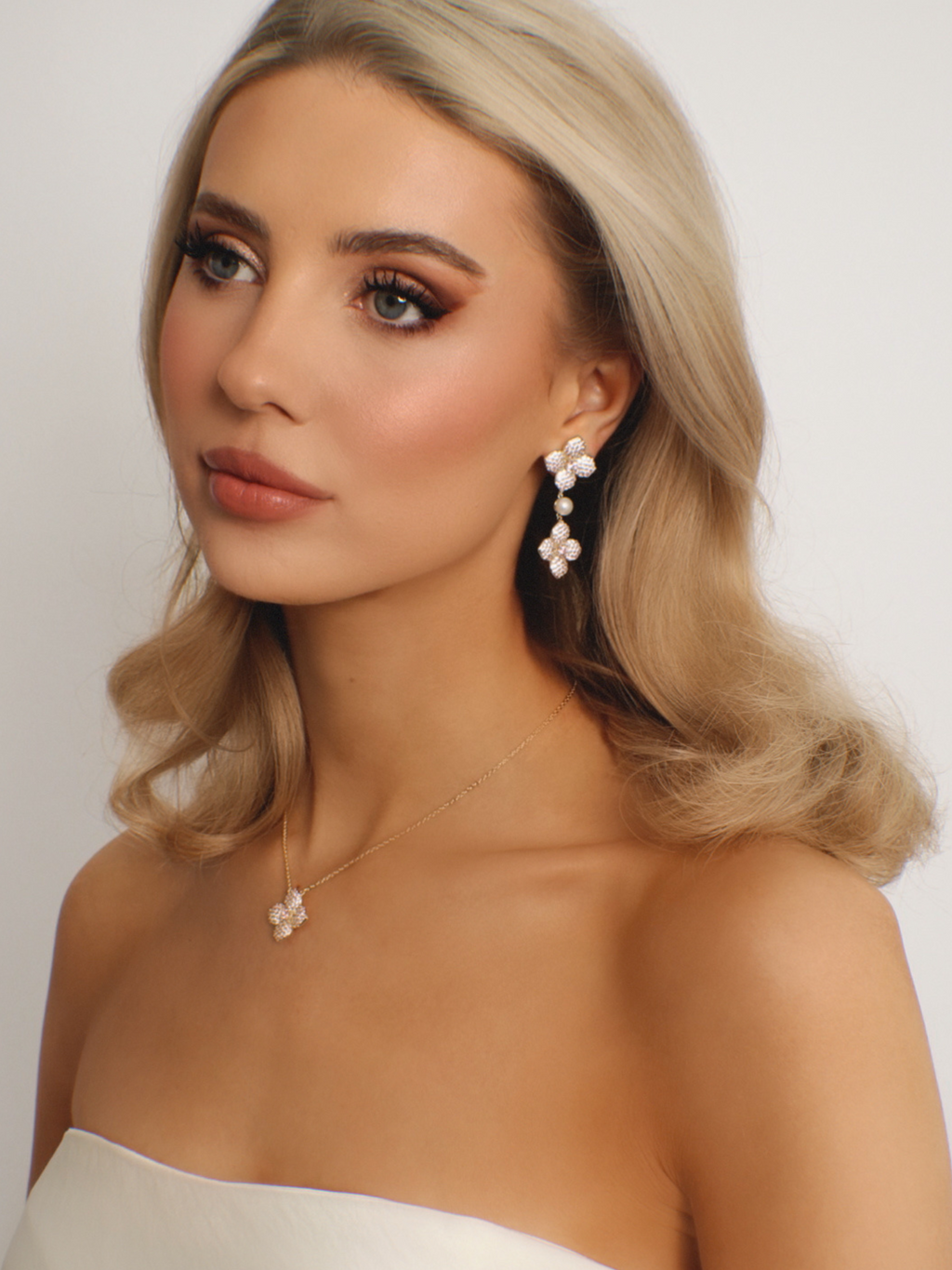 Model wearing gold-plated hydrangea earrings and necklace with light pink CZ stones in elegant studio portrait