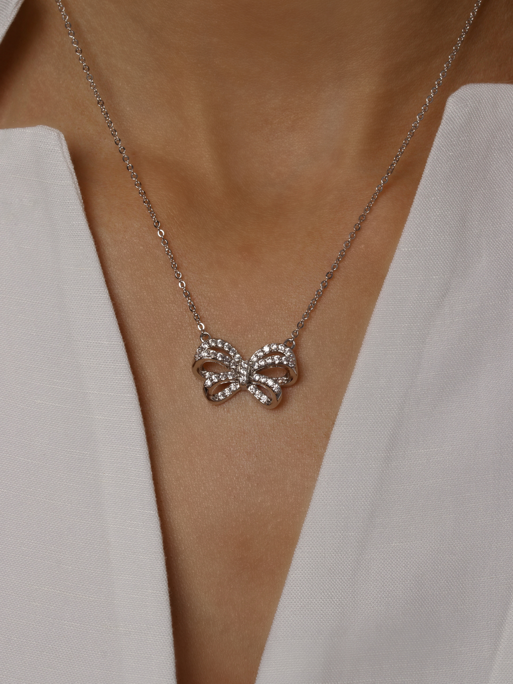 Meredith Bow Necklace in premium White Gold plating with crystal pavé bow pendant, worn on model with white blouse