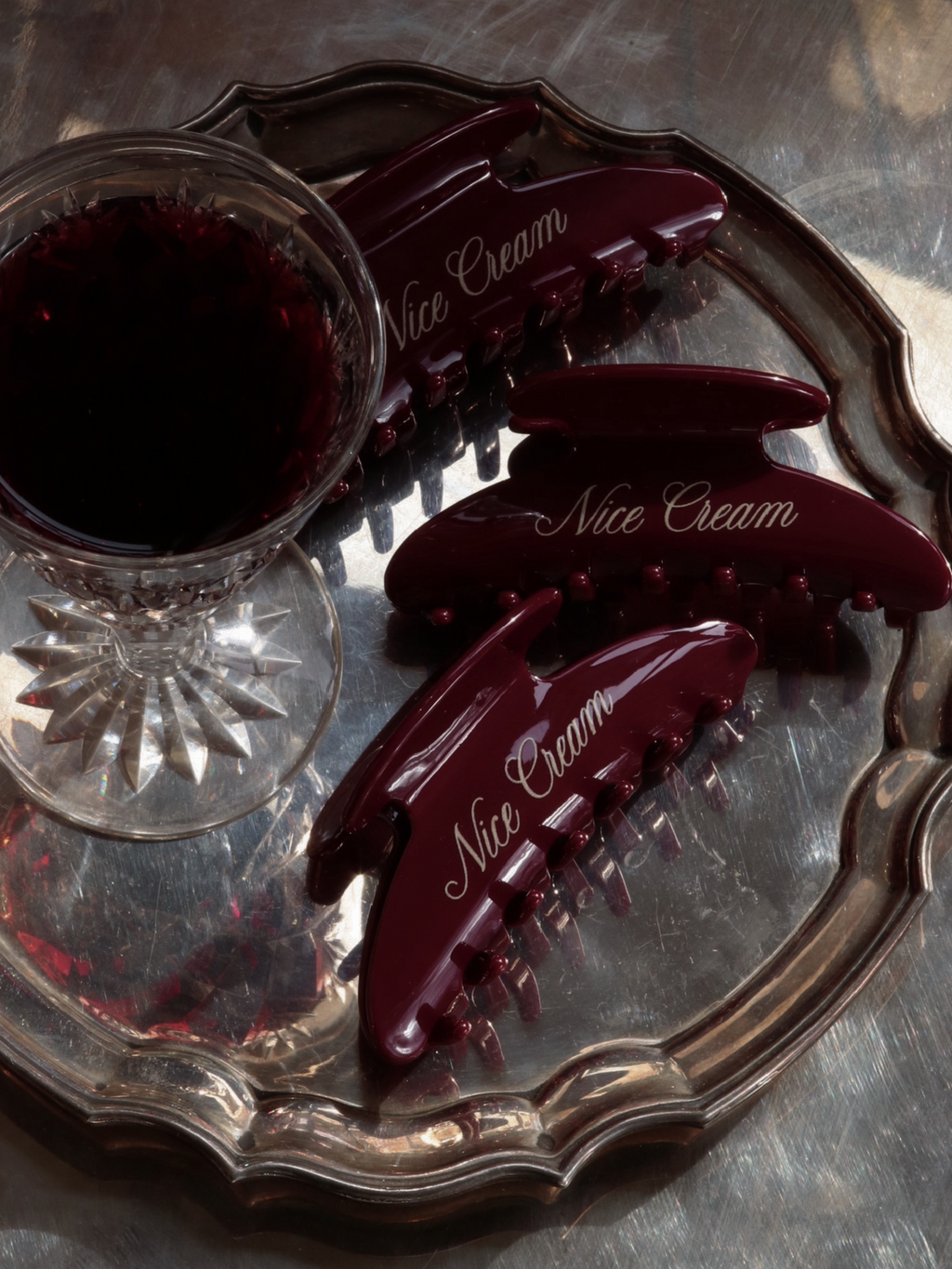 Overhead shot of merlot claw clips on a silver tray beside a crystal cut glass of red wine.