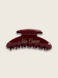 Flat-lay of a merlot claw hair clip on white background featuring brand name, showcasing affordable luxury and timeless British elegance.