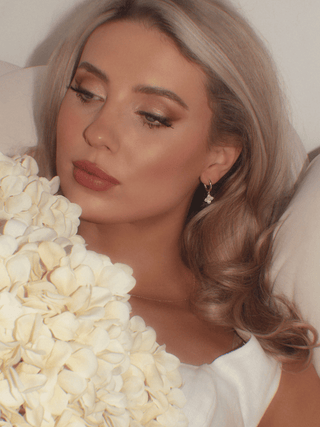 Gold Mini Hydrangea hoop earrings worn by reclining model with soft curls, floral background and dewy makeup, showcasing luxurious yet affordable flower-inspired jewellery.