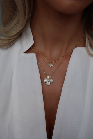 Model wearing layered gold necklaces featuring the Mini Hydrangea pendant and a larger pavé flower pendant against a deep V white blouse