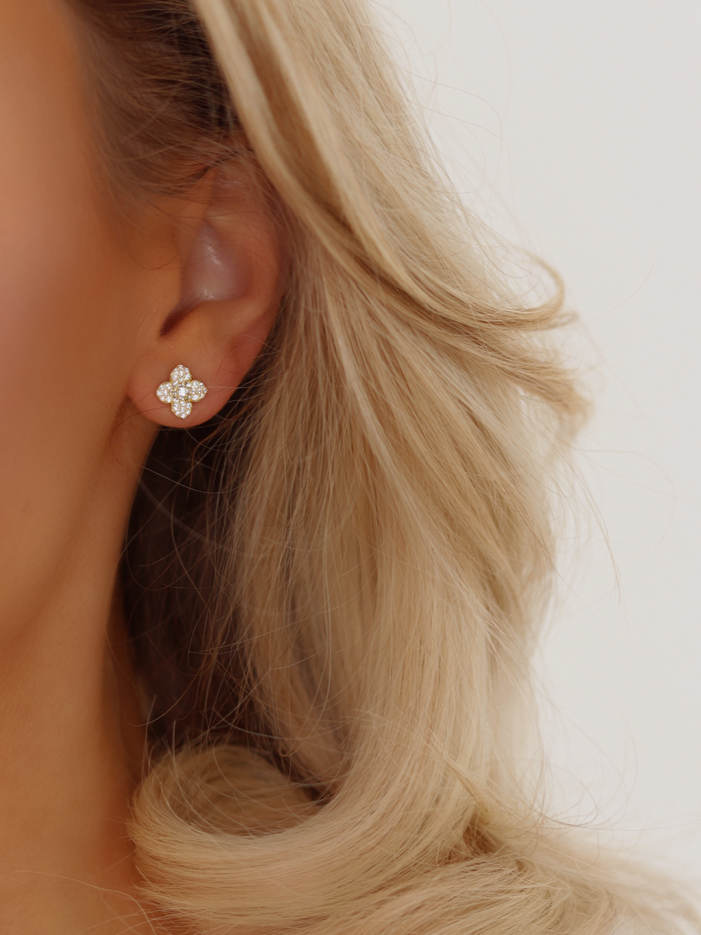 Gold plated Mini Hydrangea stud earring worn by model, showing a dainty pavé floral design against blonde hair and soft lighting