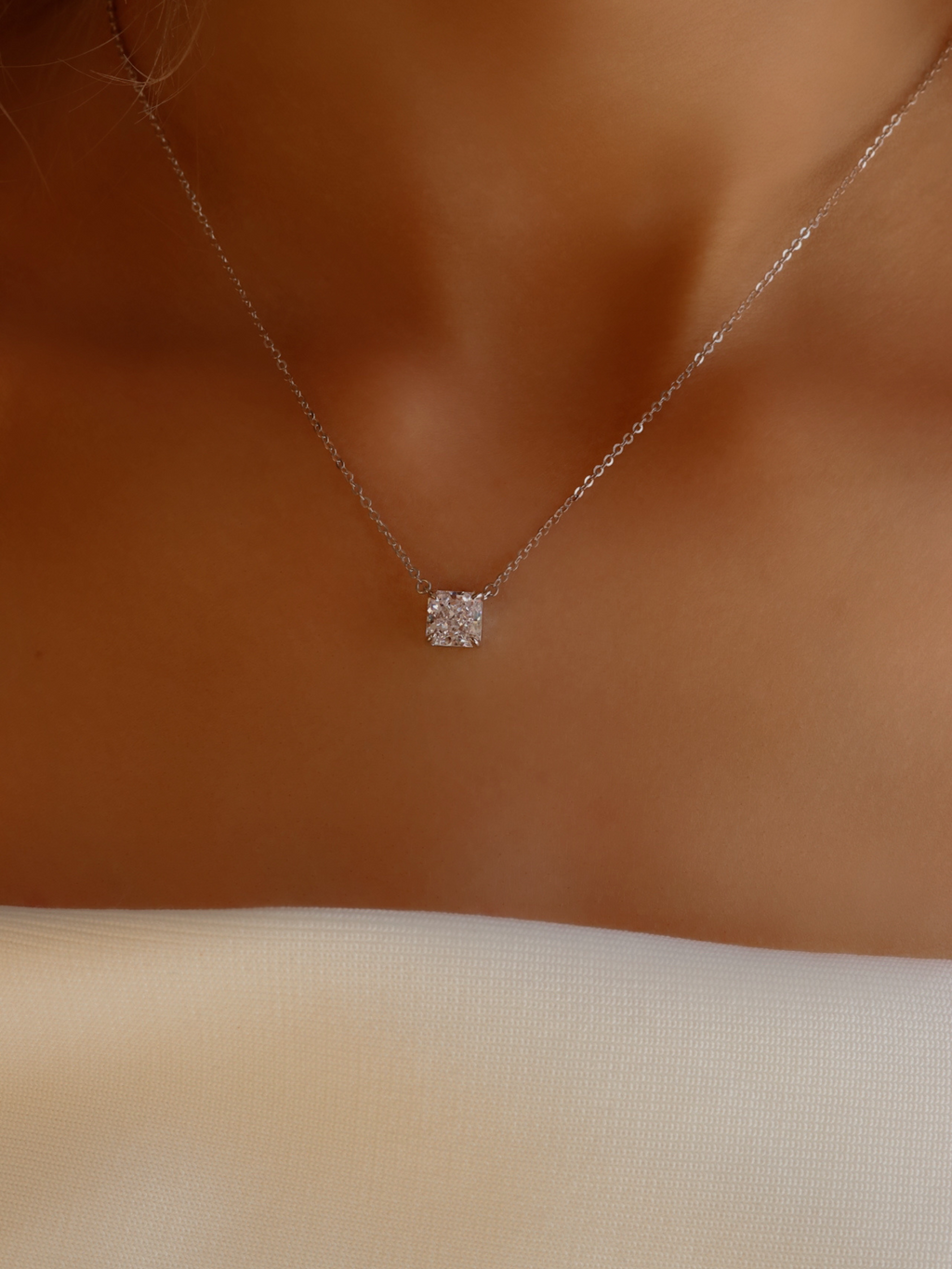 Close-up of the Regina necklace worn with a white dress, showcasing the minimalist square-cut CZ stone and fine sterling silver with white gold plating for a sophisticated, understated style.