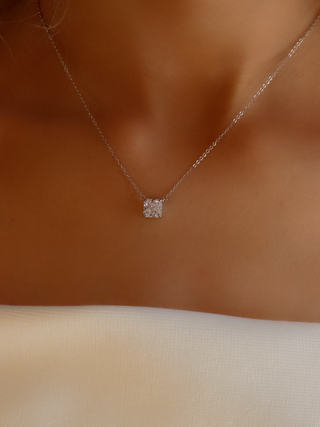 Close-up of the Regina necklace worn with a white dress, showcasing the minimalist square-cut CZ stone and fine sterling silver with white gold plating for a sophisticated, understated style.