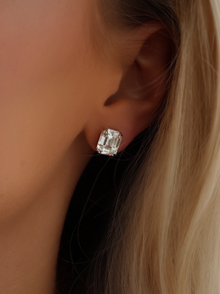 Close-up of Seraphina emerald-cut CZ stud earrings in white gold plated sterling silver, worn by blonde-haired model, showcasing modern geometric style and elegant sparkle.